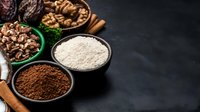 Assorted baking ingredients in bowls on dark background including cocoa powder, flour, nuts and cinnamon sticks, with copy space for recipe or menu design.