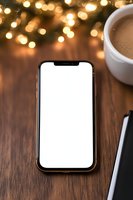 Smartphone with blank white screen on wooden table with coffee cup and bokeh lights background, mockup for app or website presentation.