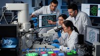 Team of diverse scientists in white lab coats collaborating on microscopic research with advanced laboratory equipment and digital displays in modern facility.
