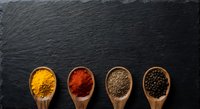 Colorful spices in wooden spoons on dark slate background. Turmeric, paprika, ground pepper and peppercorns arranged for culinary cooking and seasoning.