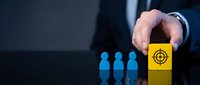Businessman hand placing yellow cube with target icon near blue human figures on dark background, symbolizing recruitment strategy.
