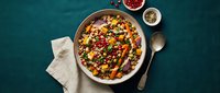Colorful bean salad with mixed legumes, corn, peppers and herbs in ceramic bowl on teal background. Healthy vegetarian meal for nutrition and wellness.