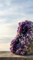 Purple amethyst crystal cluster on wooden surface against cloudy sky background for healing meditation and spiritual wellness practices.
