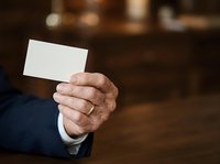 Senior male professional in dark business suit holding blank white card for contact information or branding mockup in office setting.