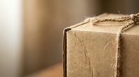 Brown cardboard package tied with natural jute rope string on wooden surface, shipping delivery box for online commerce and postal services.
