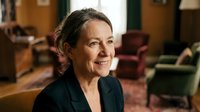 Professional mature Caucasian businesswoman smiling confidently in elegant office setting with warm lighting and classic furniture background.