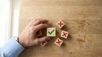 Hand selecting wooden cube with green checkmark from group of blocks showing red crosses on natural wood surface for decision making concepts.