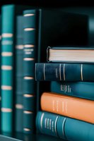 Stack of vintage hardcover books in teal and orange colors on wooden shelf, with selective focus on book spines showing classic binding details and gold lettering.