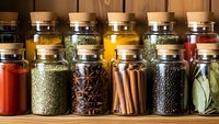 Colorful spices and herbs in glass jars with cork lids arranged on wooden shelf for cooking, seasoning, culinary arts and kitchen organization.