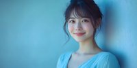 Young Asian woman with gentle smile wearing light blue dress against turquoise wall background, soft natural lighting creates dreamy atmosphere for lifestyle and beauty content.