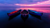Three wooden canoes floating on calm lake water reflecting vibrant purple and pink sunset sky, creating mirror-like symmetry in dramatic twilight atmosphere.
