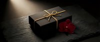 Elegant black gift box with golden ribbon and red orchid flower on dark slate surface with dramatic lighting for luxury presentation and special occasions.