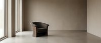 Minimalist interior space with single dark leather armchair positioned near large window, concrete flooring, neutral beige walls, modern architectural design for contemporary home decor projects.