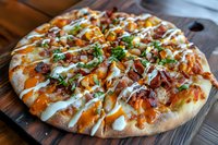 Gourmet pizza topped with pulled pork, melted cheese, drizzled with buffalo and ranch sauces, garnished with fresh herbs on wooden serving board.