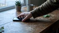 Person's hand using computer mouse on wooden desk with succulent plant and coffee mug by window, suitable for business, technology, and workspace concepts.