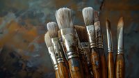 Artist paintbrushes with wooden handles and natural bristles against dark textured background, showing wear and paint stains from creative use in studio setting.