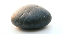 Smooth dark gray river stone with natural texture and water droplets isolated on white background for spa wellness meditation zen design projects.