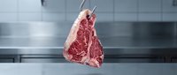 Raw beef steak hanging in professional kitchen with stainless steel background, suitable for culinary, restaurant, and food industry marketing materials.