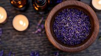 Dried lavender flowers in wooden bowl with glowing candles on rustic table. Aromatherapy and spa wellness concept with natural organic herbs.