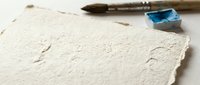 Handmade textured paper with deckled edges and paintbrush with blue watercolor paint for artistic projects and creative writing applications.