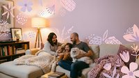 Happy family with toddler and fluffy dog relaxing on couch in cozy living room with decorative wall art and warm lighting for lifestyle content.