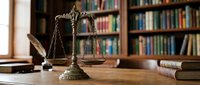 Golden scales of justice on wooden desk in law library with legal books and gavel for attorney office and courtroom concepts.