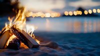 Cozy beach bonfire with burning logs on sandy shore at dusk, glowing bokeh lights reflecting on water surface creates romantic evening atmosphere.