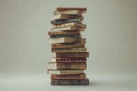 Stack of vintage hardcover books with worn leather bindings arranged in uneven tower against neutral background, creating dramatic shadows and textures.