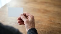 Senior male hand holding blank white business card on wooden surface with natural sunlight for corporate branding and marketing purposes.