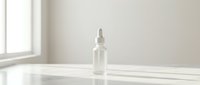 Clear glass dropper bottle with serum or essential oil on white surface with natural window light, suitable for cosmetics, skincare, and wellness product packaging design.