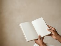 Open book with blank pages held by hands against neutral beige background, suitable for publishing, education, and creative projects.