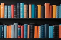 Colorful hardcover books arranged on dark wooden shelves creating vibrant pattern of spines in blue, orange, and red tones against black background. Perfect for education themes.