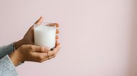 Person of South Asian descent holding a glass of milk against a soft pink background, suitable for dairy product marketing, nutrition content, and wellness advertising.