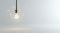 Glowing light bulb with technology icons floating around in modern minimalist interior space representing innovation and creative ideas for business.