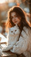 Young woman with long brown hair holding white fluffy cat in cozy knit sweater during golden hour sunset, creating warm atmospheric portrait.