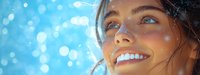 Young Caucasian woman with bright smile and blue eyes looking up at snowy sky, winter portrait with bokeh lights and natural sunlight creating magical atmosphere.