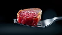 Juicy medium rare beef steak piece on silver fork against dark background, close up view showing tender meat texture and pink center for restaurant menu.