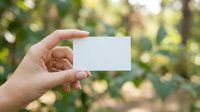 Hand holding blank white business card outdoors with green bokeh nature background, mockup with copy space for text or logo.