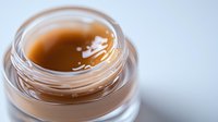 Golden honey or amber skincare serum in open glass jar with smooth glossy texture for natural beauty and wellness cosmetic products.