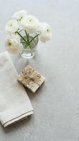 White ranunculus flowers in glass vase with wrapped gift and linen napkin on neutral background for home decor and lifestyle photography.