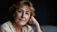 Thoughtful mature Caucasian woman with short blonde hair resting chin on hand against dark background, conveying wisdom and contemplation for lifestyle content.