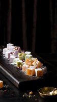 Assorted Turkish delight lokum confections with nuts and rose petals on wooden board, traditional Middle Eastern sweets for dessert photography.