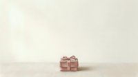 Small rose gold gift box with ribbon bow on neutral beige background, isolated for holiday, celebration, and packaging design projects.