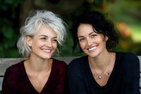 Two happy women friends laughing together outdoors in natural light. Diverse female friendship, bonding moment between mature and young adults.