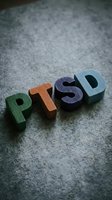 Colorful wooden letter blocks spelling PTSD arranged on gray concrete surface, representing post-traumatic stress disorder awareness and mental health education.