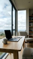 Modern home office workspace with wooden desk, laptop, and coffee mug overlooking expansive landscape through floor-to-ceiling windows, featuring comfortable seating and built-in shelving for remote work.