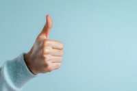 Close-up of hand showing thumbs up gesture wearing light blue sweater sleeve against pastel blue background, expressing positivity and approval in minimal style.