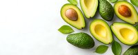 Fresh ripe avocados cut in half showing golden flesh and brown pit, whole green fruits and leaves arranged on white background with copy space.
