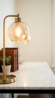 Brass table lamp with amber glass globe shade and illuminated bulb on marble surface, modern home decor and interior design lighting fixture.