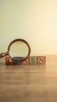 Vintage wooden alphabet blocks spelling LEARN with magnifying glass on wood table for education and discovery concepts.